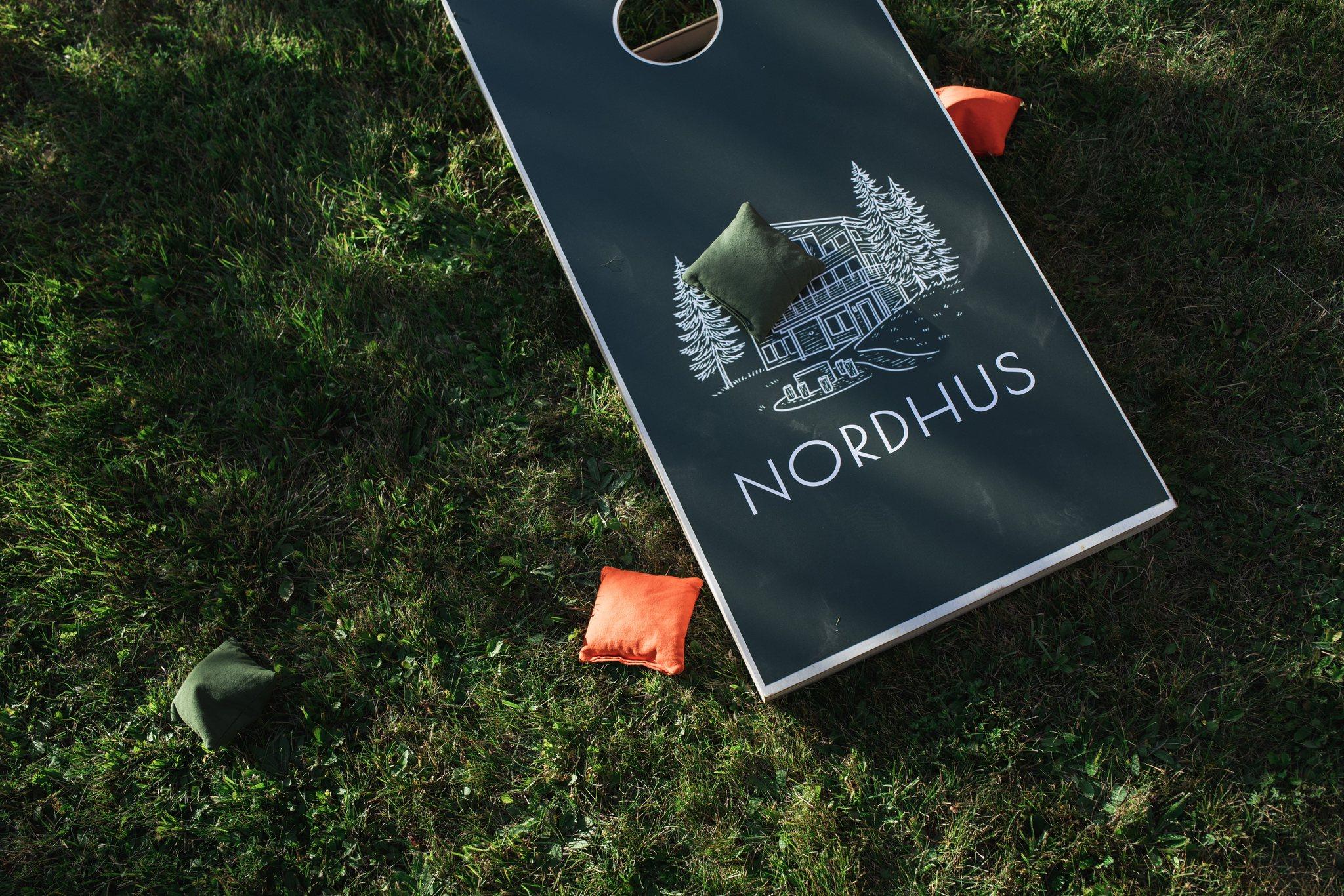 Custom Nordhus-branded cornhole board and bags on the summer lawn at Nordhus Lodge