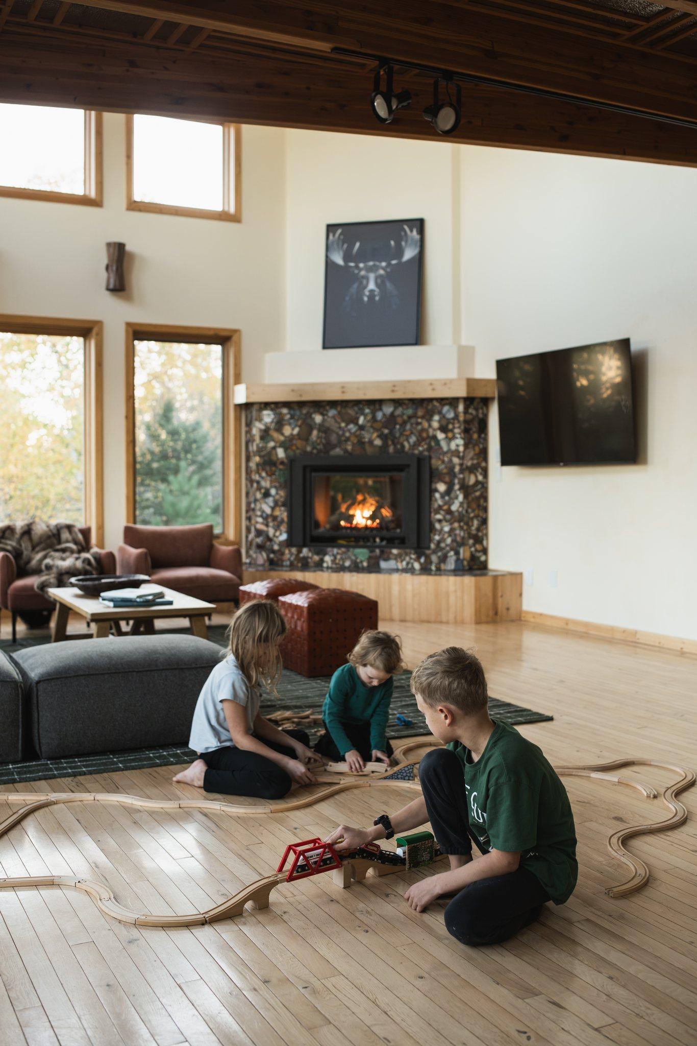 Children playing on the floor by the lit stone fireplace at Nordhus Lodge