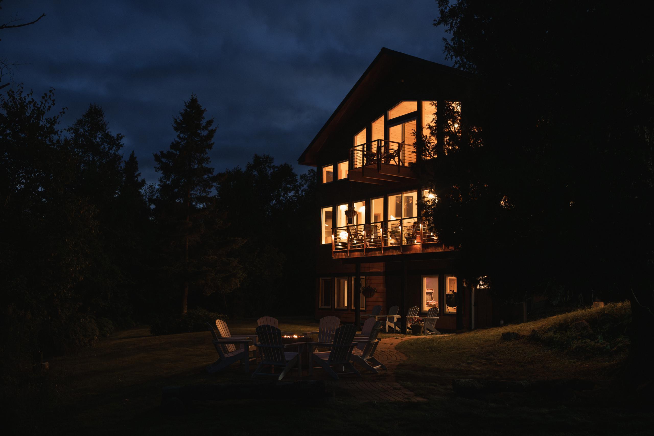 Nordhus Lodge aglow at dusk with the lakeside fire pit lit, surrounded by North Shore forest in Lutsen, Minnesota