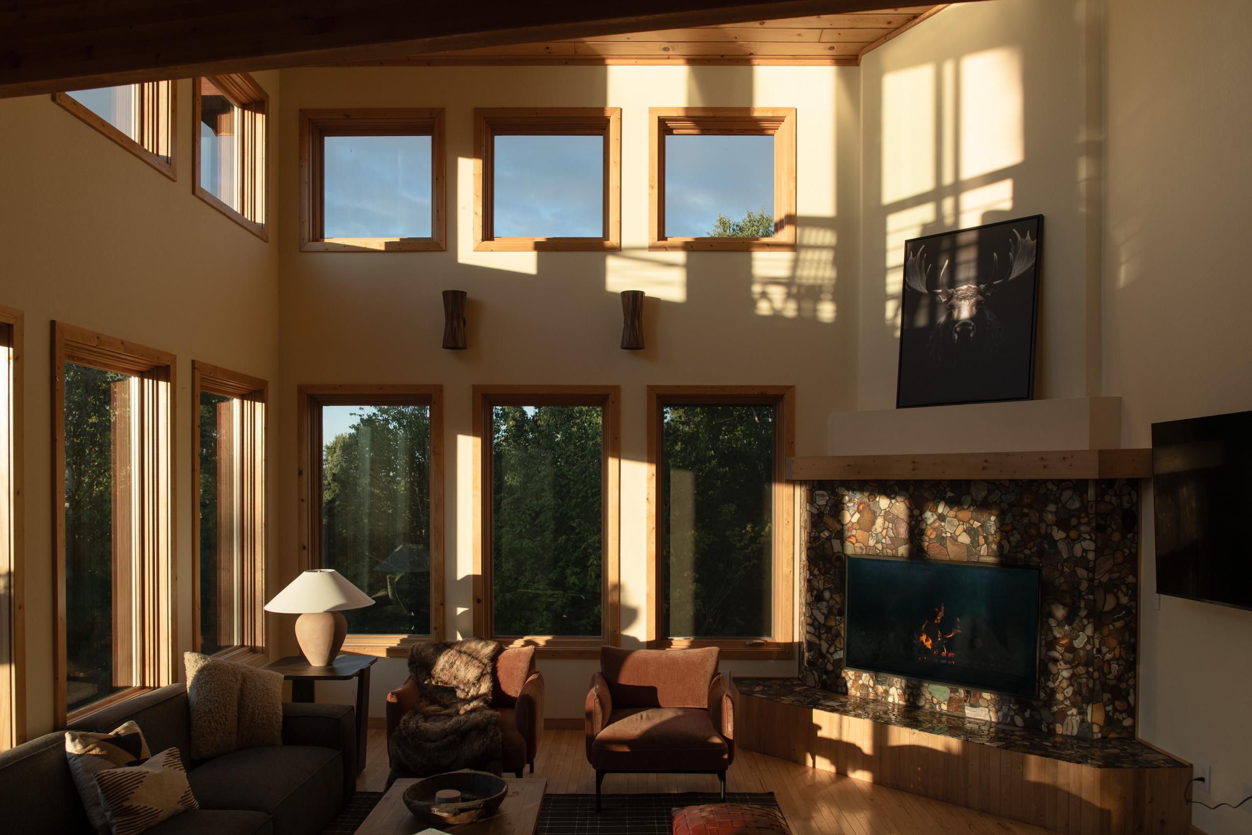 Great room with a stone fireplace and wall of windows at golden hour at Nordhus Lodge